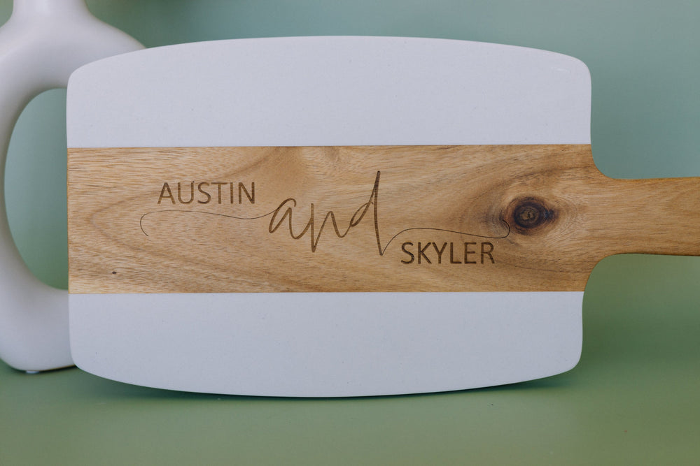 White cutting board with wooden handle engraved with 'Austin and Skyler' on a green background