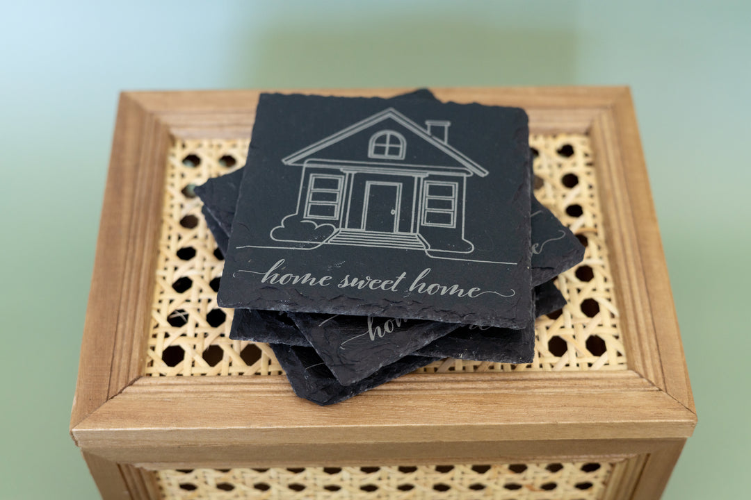 Stack of coasters with house design and 'home sweet home' text on a wooden box.