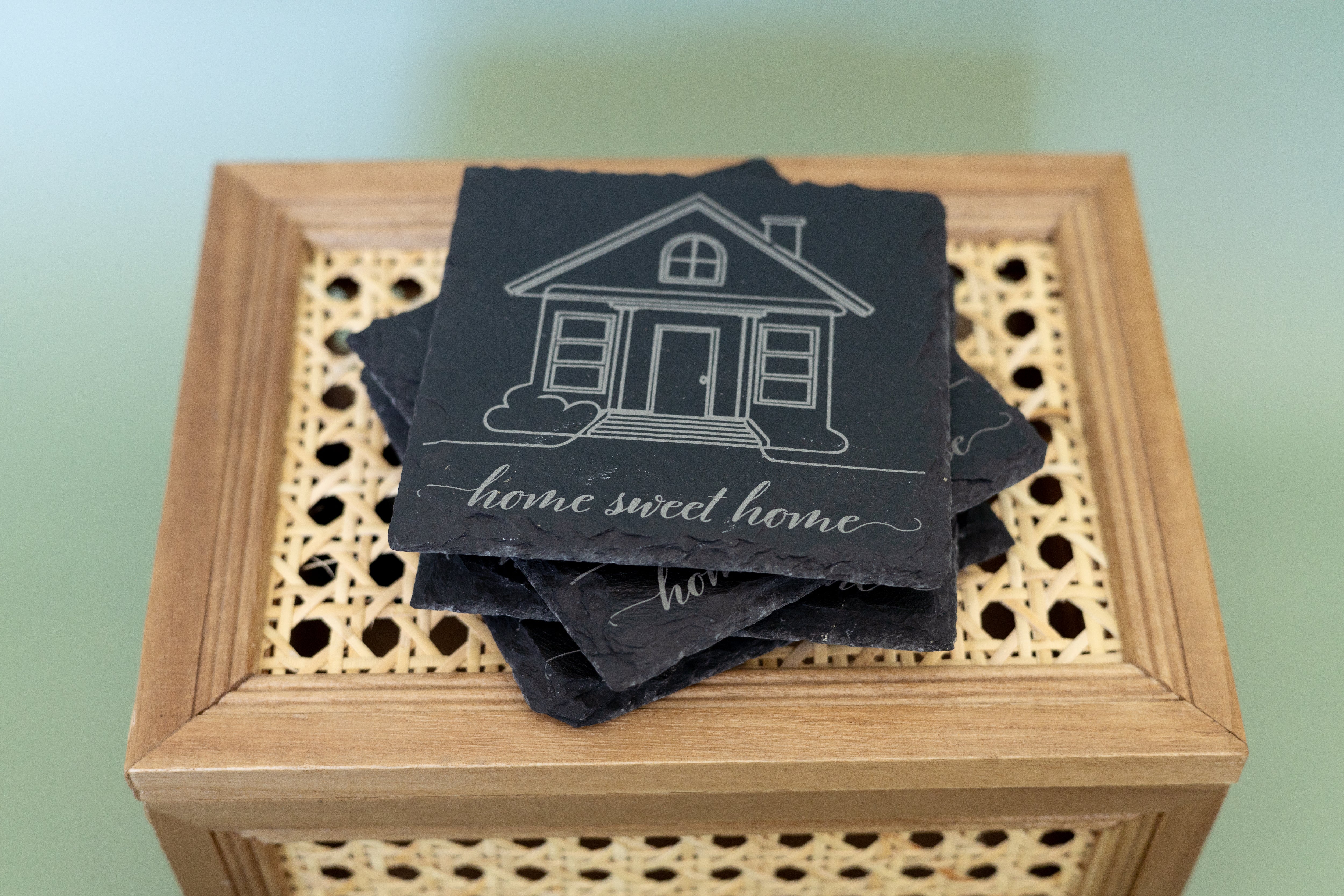 Stack of coasters with house design and 'home sweet home' text on a wooden box.