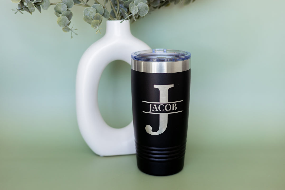 Black tumbler with 'JACOB' engraving next to a white vase on a light green background